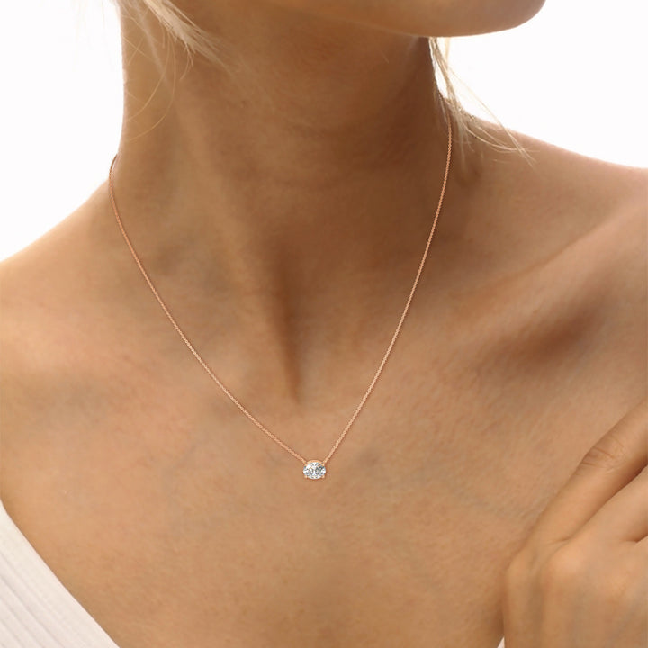 Rose gold necklace with a diamond pendant on a person's neck against a white background