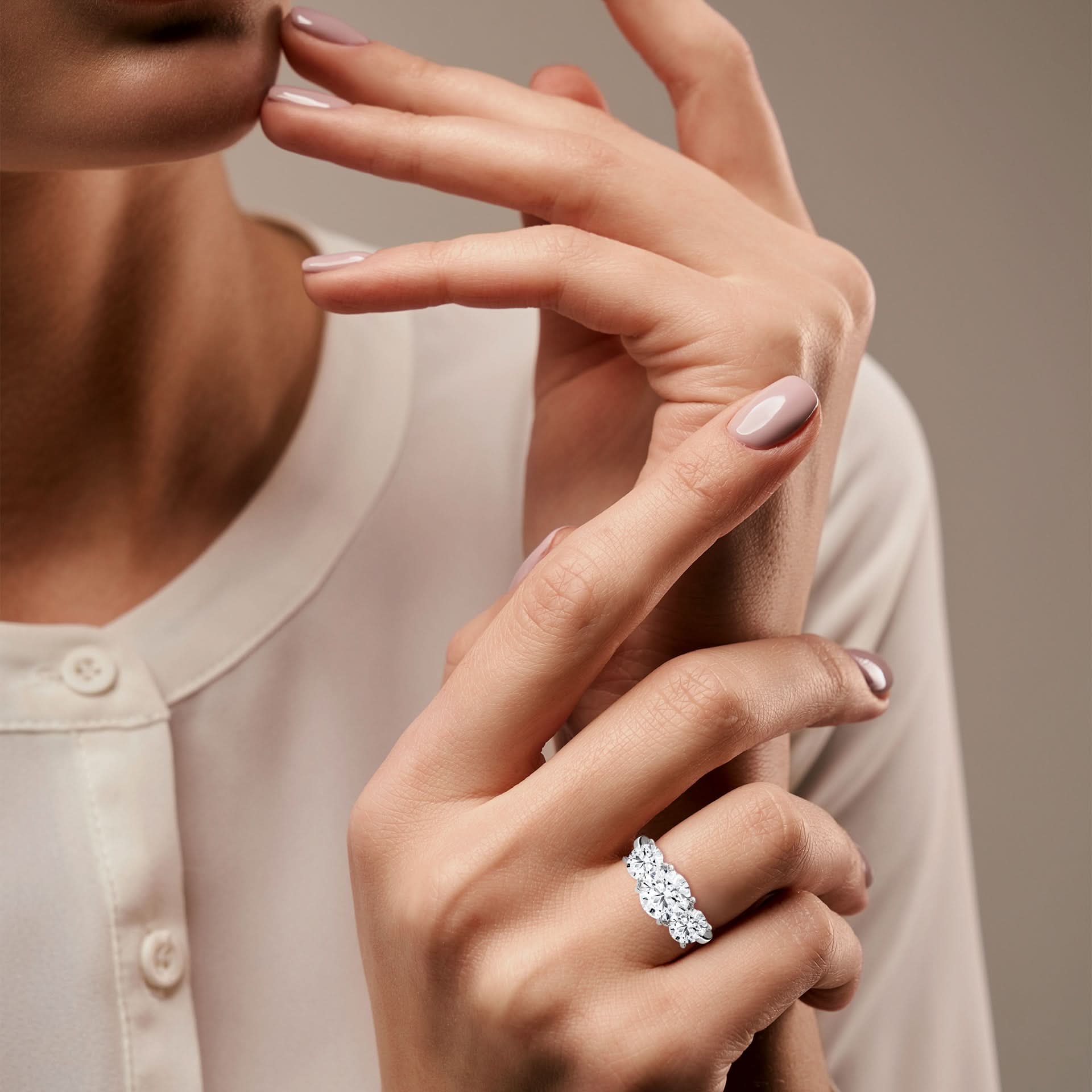 Close-up of a woman's hand wearing a diamond ring on a neutral background