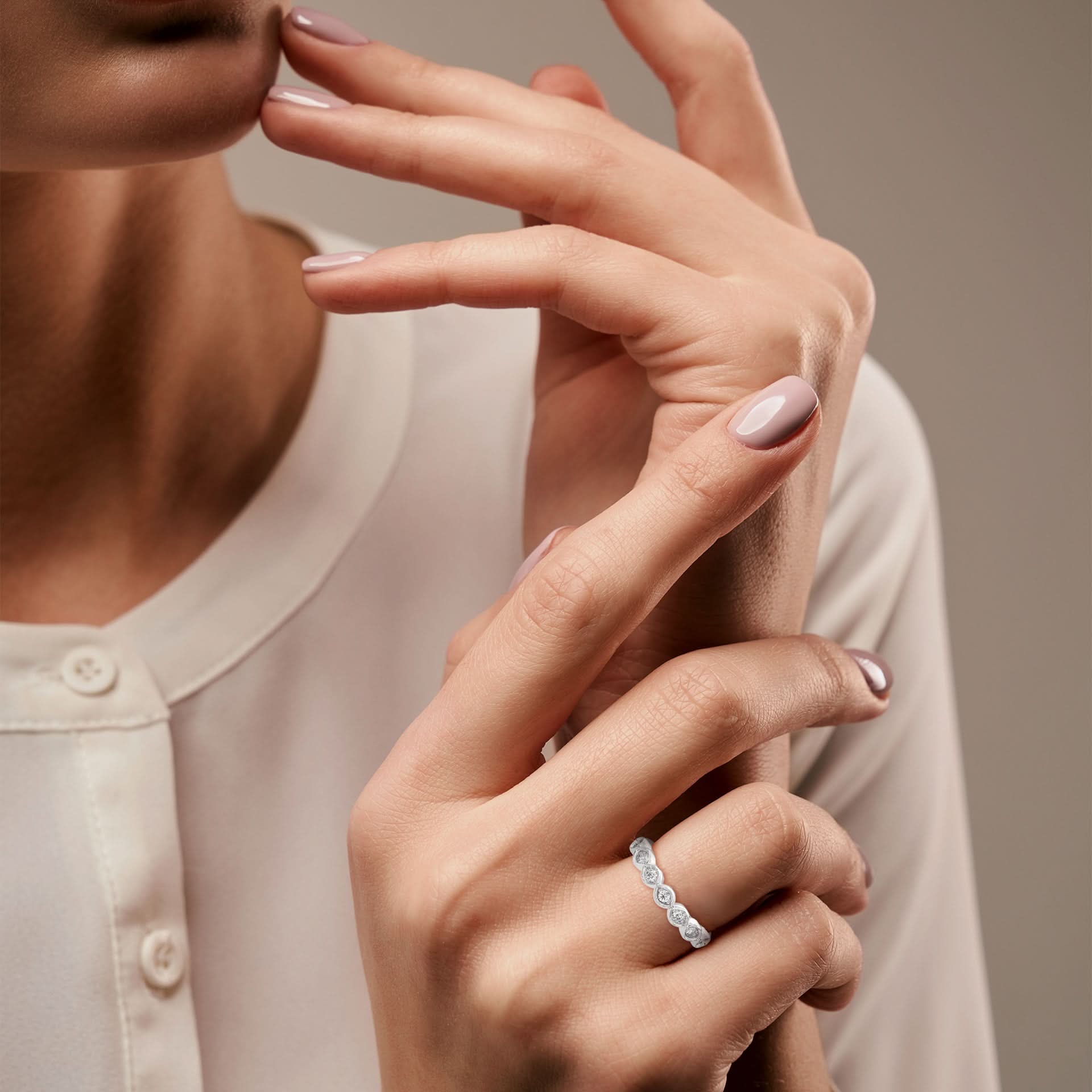 Close-up of a woman's hands with a silver ring on a neutral background