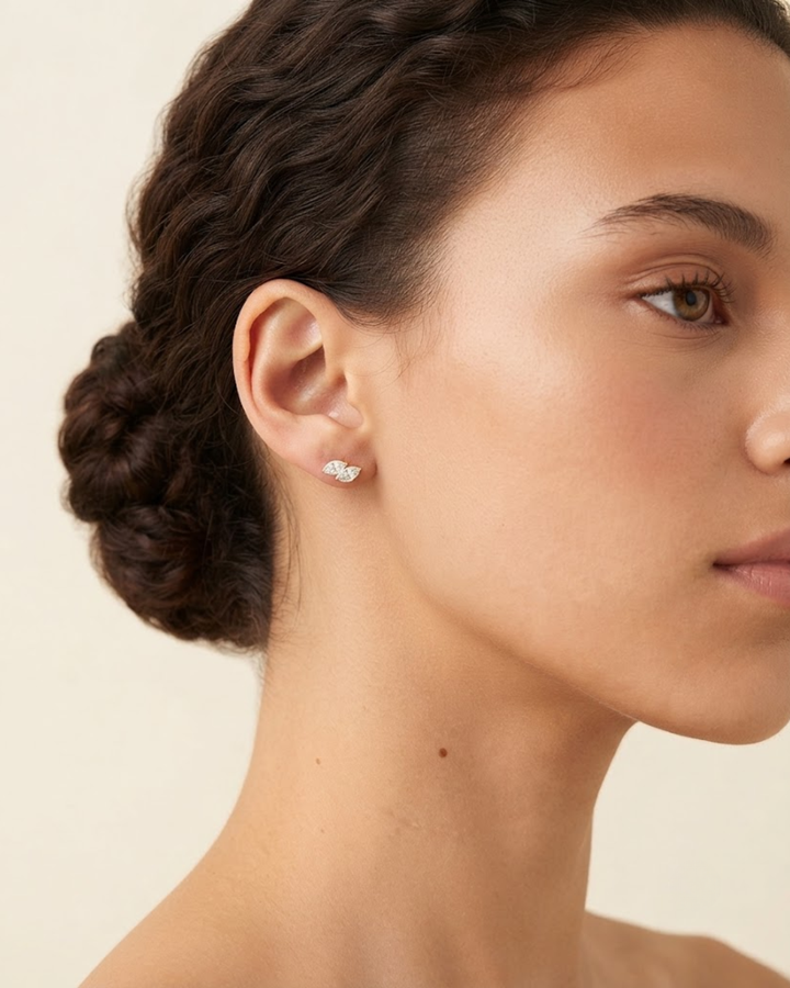 A close-up side profile of a woman wearing a small silver stud earring with a clear crystal cluster, set against a plain light beige background.