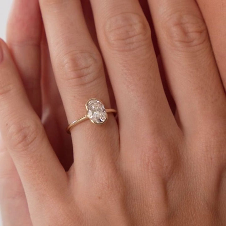 A close-up of a hand wearing a delicate gold ring with an oval clear gemstone.