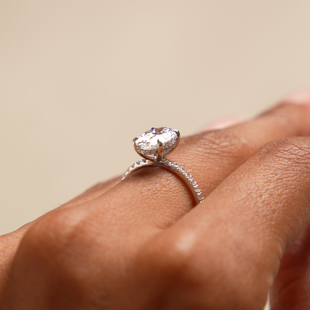 Oval shaped diamond ring on a finger against a neutral background