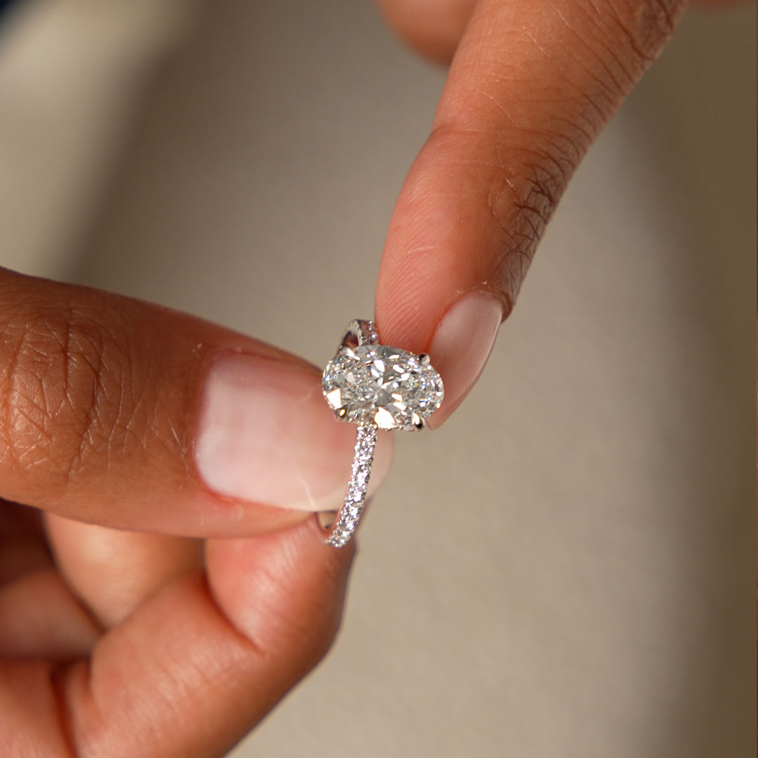 Diamond ring held between fingers against a neutral background