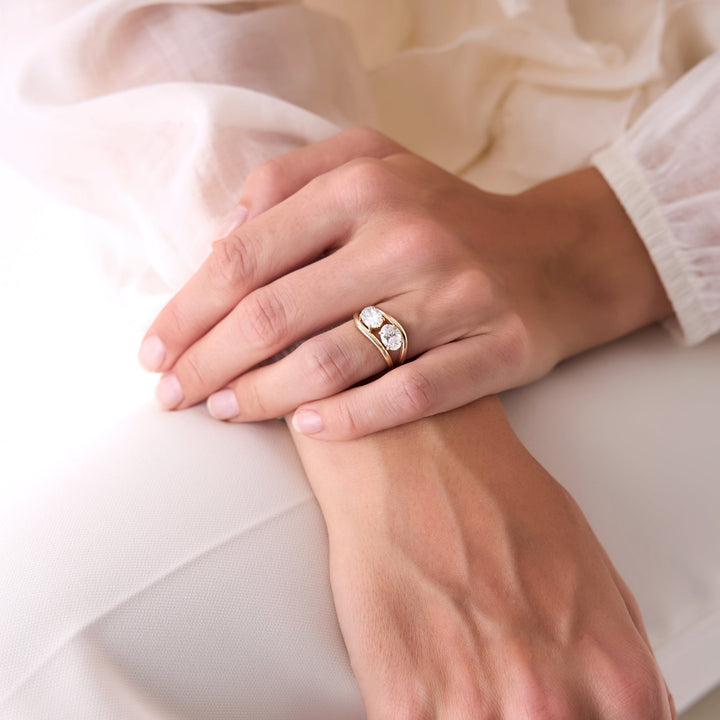 Close-up of a hand wearing a gold ring with two diamonds on a light background
