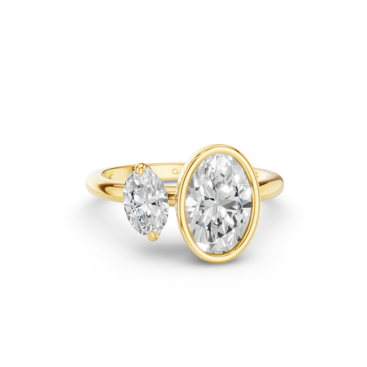 A yellow gold ring featuring a large oval-cut diamond on the right and a smaller marquise-cut diamond on the left, set on a plain white background.