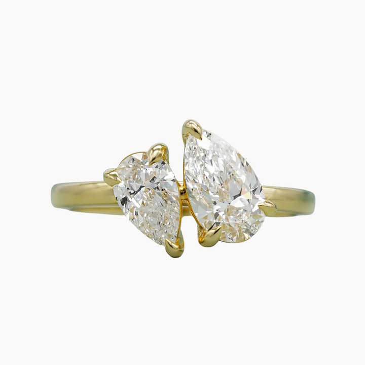 Gold ring with two pear-shaped diamonds on a white background