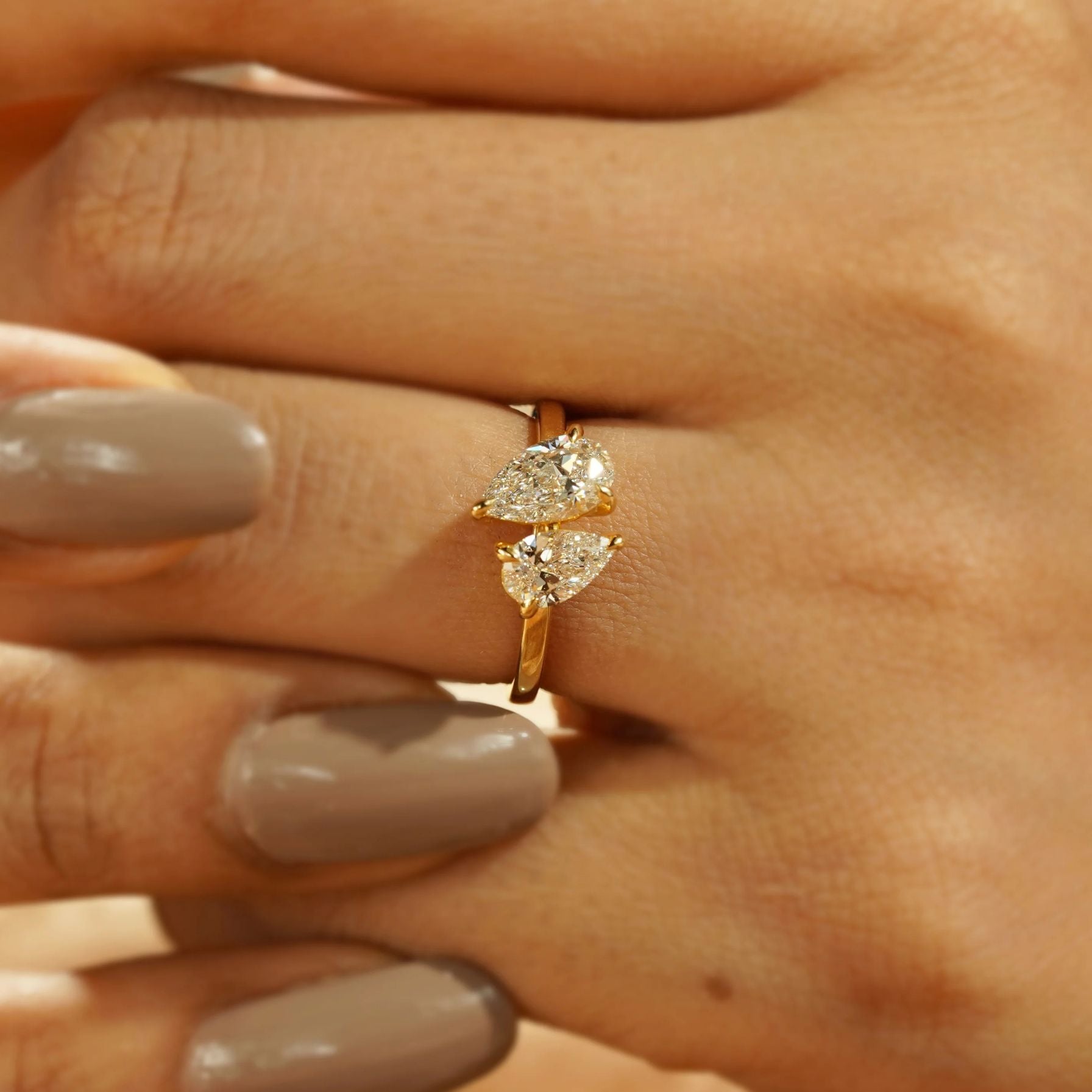 Gold ring with two pear-shaped diamonds on a hand with gray nail polish.
